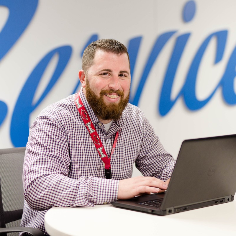 A Walmart Services Associate sits in the office with his laptop. 