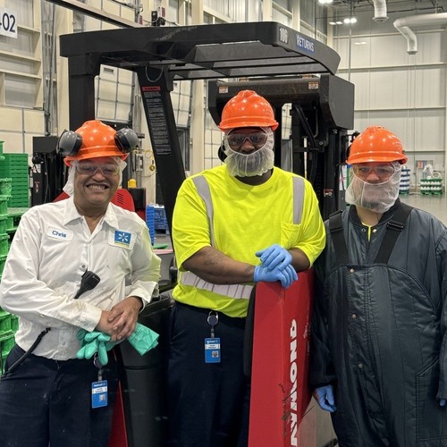 Three workers standing in front of a fork lift